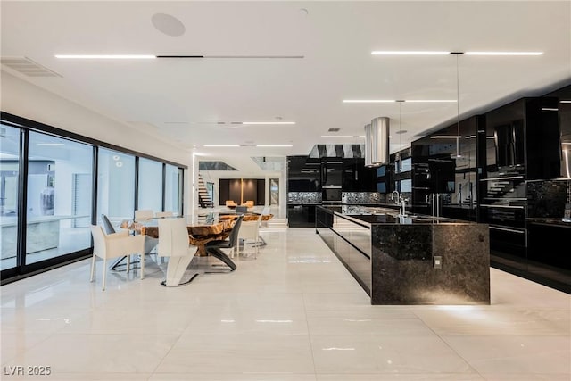 kitchen featuring oven, a kitchen island with sink, and dark stone countertops