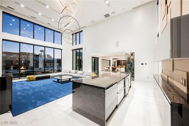 interior space featuring a spacious island, white cabinets, decorative light fixtures, dark stone counters, and a chandelier