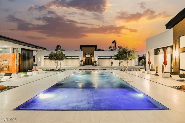 pool at dusk featuring a patio area and pool water feature