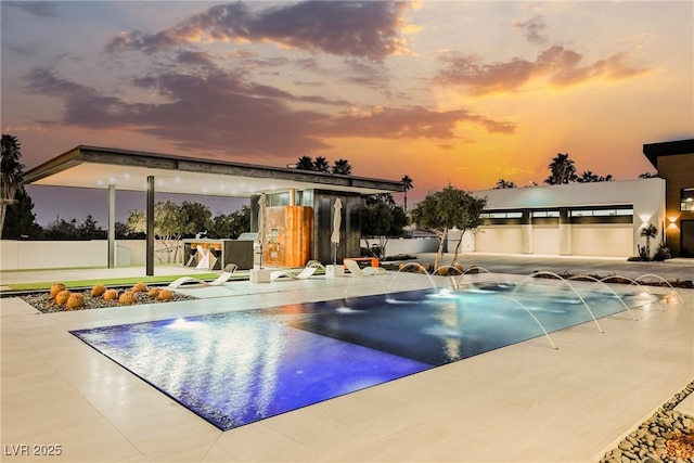 pool at dusk featuring pool water feature and a patio area