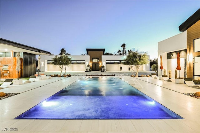 pool at dusk with pool water feature and a patio area