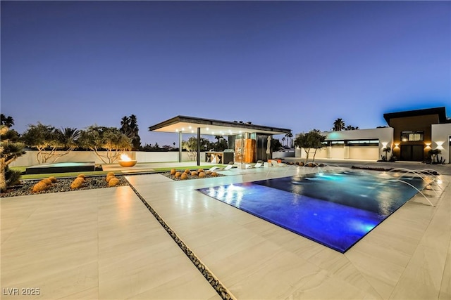 pool at dusk with pool water feature and a patio area