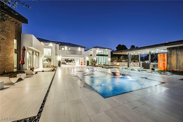 pool at night featuring a jacuzzi and a patio