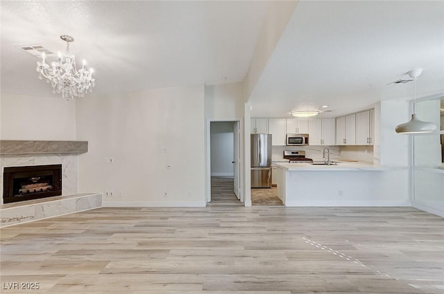 unfurnished living room with a premium fireplace, sink, a chandelier, and light hardwood / wood-style flooring