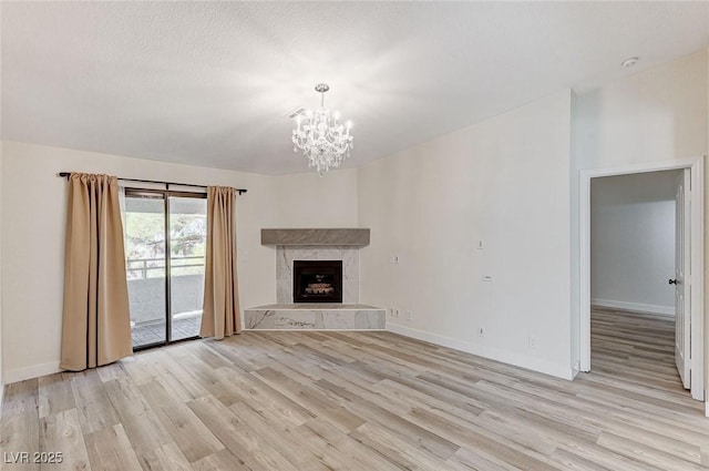 unfurnished living room with a tiled fireplace, a chandelier, a textured ceiling, and light hardwood / wood-style floors