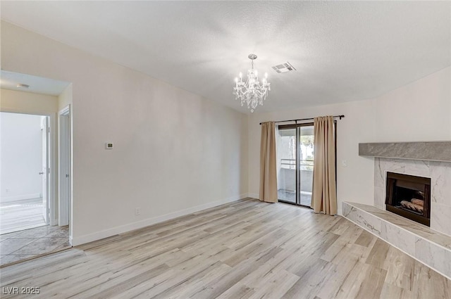 unfurnished living room with a textured ceiling, a fireplace, light hardwood / wood-style floors, and a chandelier