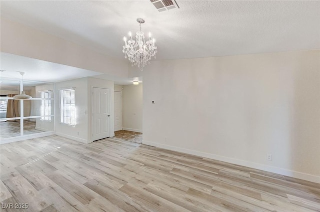 unfurnished room featuring an inviting chandelier, light hardwood / wood-style floors, and a textured ceiling