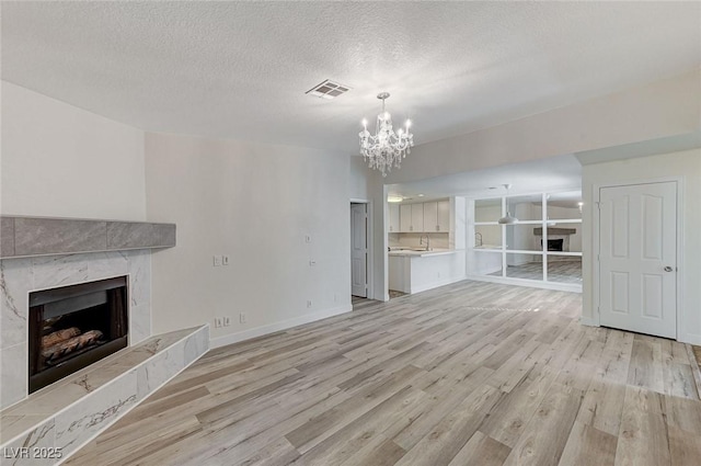 unfurnished living room featuring sink, a chandelier, a high end fireplace, a textured ceiling, and light wood-type flooring