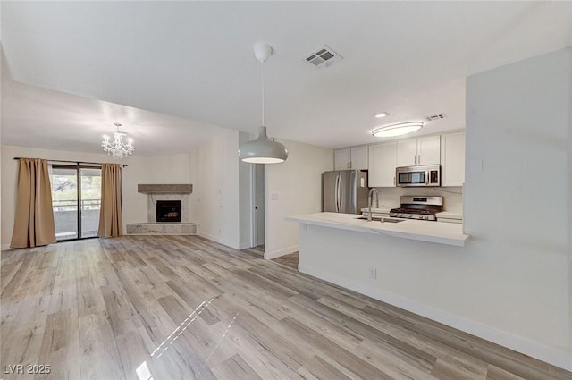 kitchen featuring appliances with stainless steel finishes, decorative light fixtures, white cabinetry, sink, and a tiled fireplace