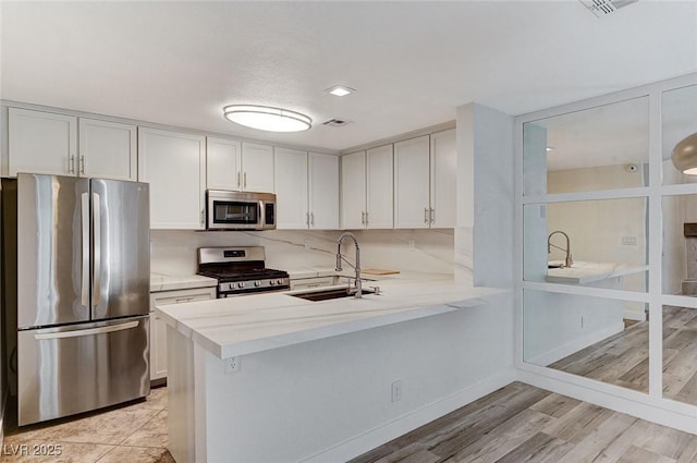 kitchen with white cabinetry, sink, kitchen peninsula, and appliances with stainless steel finishes