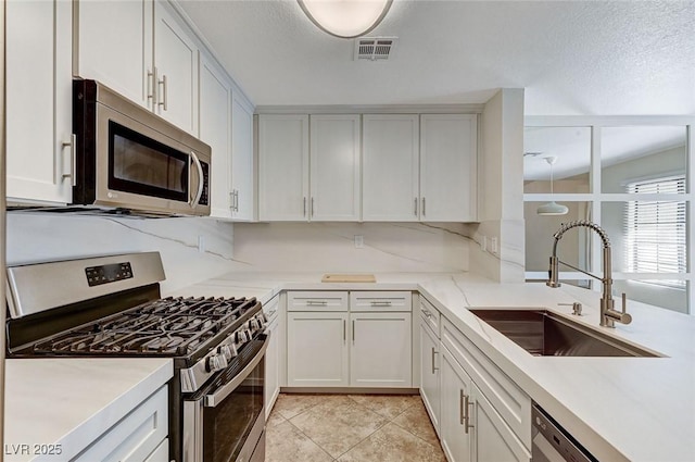 kitchen featuring sink, light tile patterned floors, appliances with stainless steel finishes, backsplash, and white cabinets