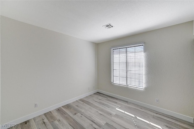 spare room with a textured ceiling and light wood-type flooring