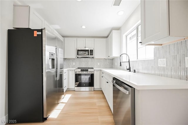 kitchen featuring sink, light hardwood / wood-style flooring, white cabinetry, stainless steel appliances, and decorative backsplash