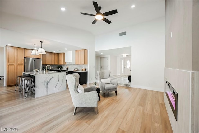 living room with ceiling fan, high vaulted ceiling, sink, and light hardwood / wood-style floors