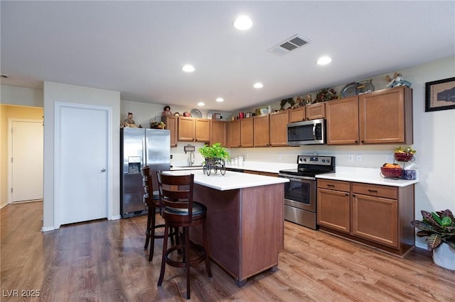 kitchen with hardwood / wood-style flooring, a kitchen island, a kitchen breakfast bar, and appliances with stainless steel finishes