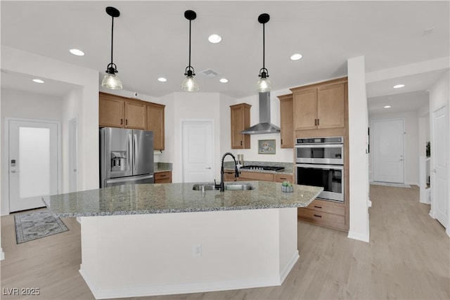 kitchen featuring sink, appliances with stainless steel finishes, light stone countertops, a kitchen island with sink, and wall chimney range hood