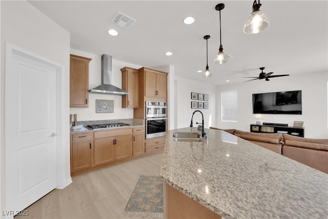 kitchen featuring pendant lighting, sink, stainless steel appliances, light stone countertops, and wall chimney exhaust hood