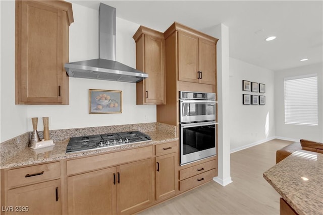 kitchen featuring light stone counters, light hardwood / wood-style flooring, light brown cabinets, appliances with stainless steel finishes, and wall chimney range hood