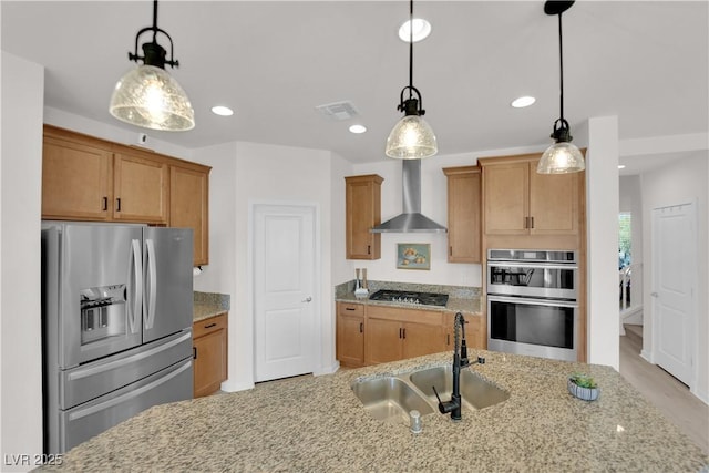 kitchen featuring decorative light fixtures, sink, stainless steel appliances, light stone countertops, and wall chimney range hood