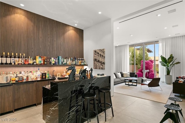 bar featuring dark brown cabinetry, wooden walls, dark stone counters, and expansive windows