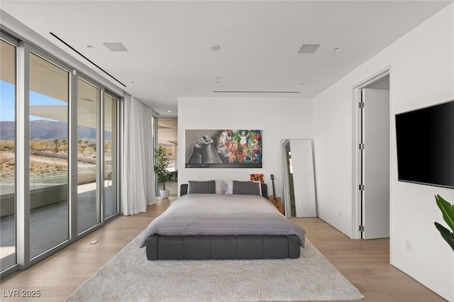 bedroom with floor to ceiling windows, access to exterior, and light hardwood / wood-style flooring