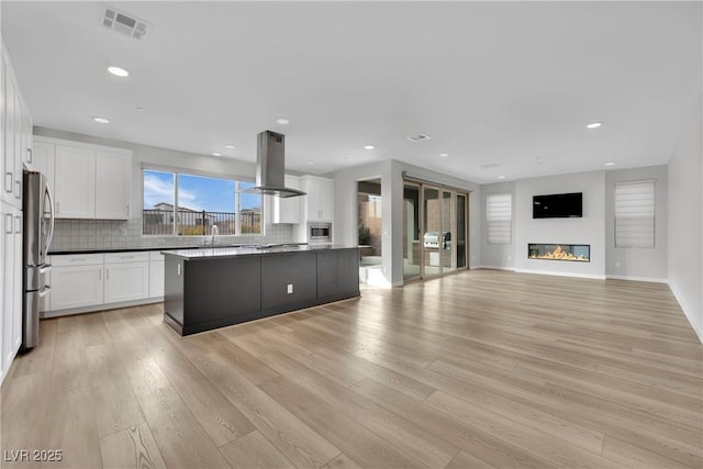 kitchen featuring appliances with stainless steel finishes, a kitchen island, white cabinets, island exhaust hood, and backsplash