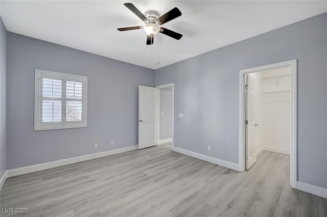 unfurnished bedroom with baseboards, a ceiling fan, wood finished floors, a walk in closet, and a closet