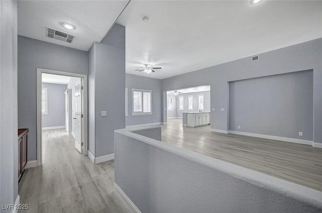 corridor with light wood-type flooring, baseboards, and visible vents