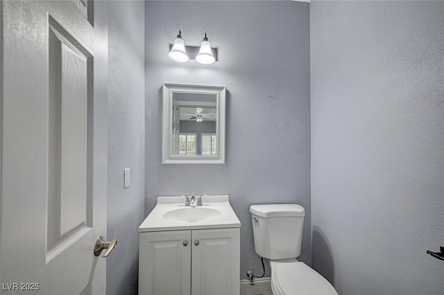 half bathroom with a textured wall, vanity, and toilet