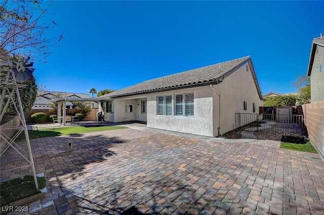 rear view of house featuring a tile roof, a patio area, a fenced backyard, and stucco siding