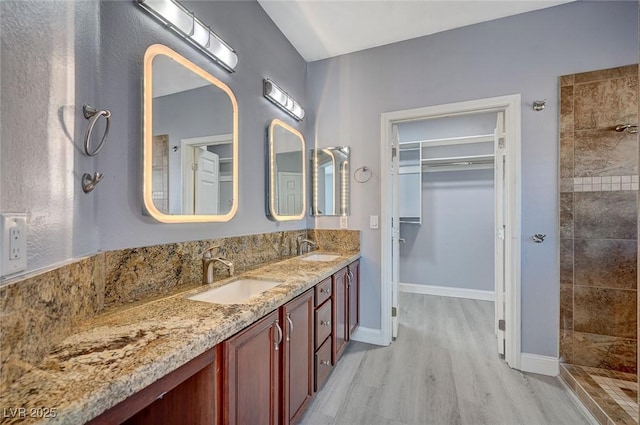 bathroom featuring double vanity, tiled shower, a sink, and wood finished floors