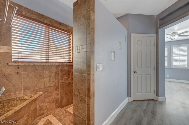 full bath with ceiling fan, wood finished floors, a tile shower, and baseboards