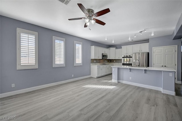 kitchen with light wood finished floors, baseboards, appliances with stainless steel finishes, light countertops, and white cabinetry