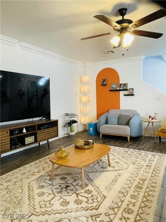 living room featuring dark wood-type flooring, ornamental molding, and ceiling fan