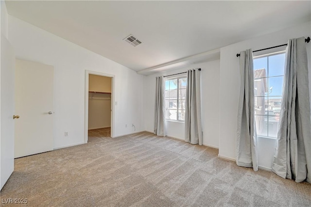 unfurnished bedroom featuring a walk in closet, lofted ceiling, and light carpet