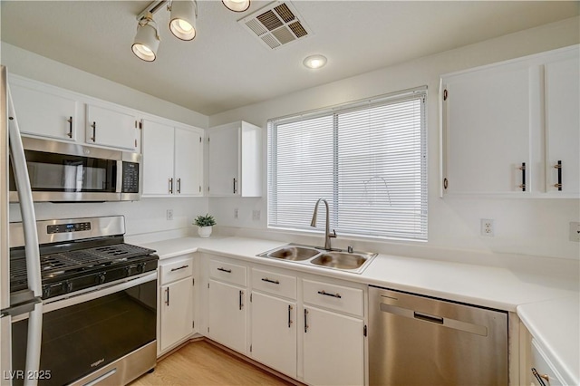 kitchen with appliances with stainless steel finishes, light hardwood / wood-style floors, sink, and white cabinets