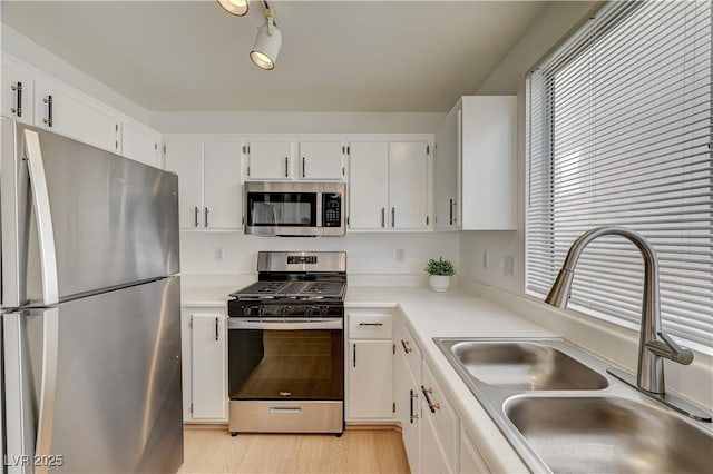 kitchen with rail lighting, sink, white cabinets, light hardwood / wood-style floors, and stainless steel appliances