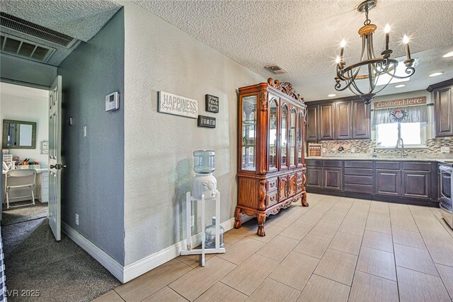 kitchen with sink, tasteful backsplash, an inviting chandelier, dark brown cabinets, and a textured ceiling