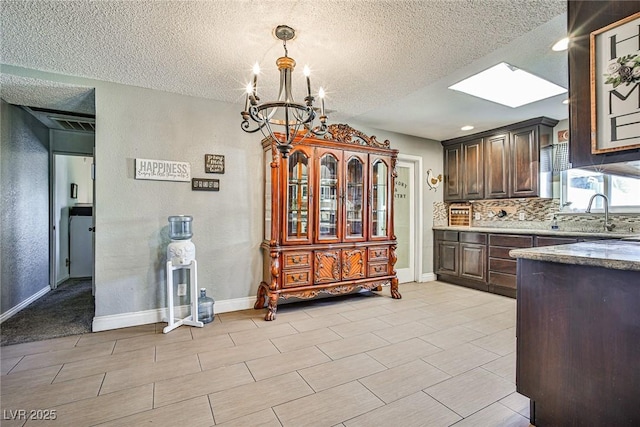 kitchen with a skylight, sink, backsplash, a notable chandelier, and dark brown cabinetry