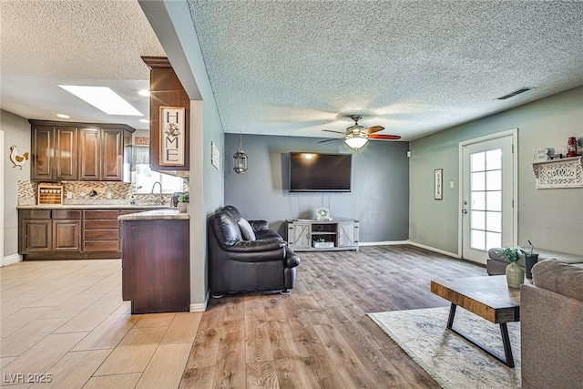 living room with ceiling fan, a textured ceiling, light wood-type flooring, and a skylight