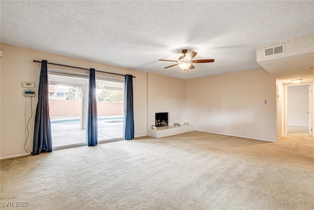 unfurnished living room featuring ceiling fan, a brick fireplace, carpet, and a textured ceiling