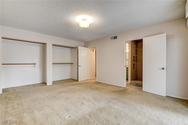 unfurnished bedroom with connected bathroom, a textured ceiling, light colored carpet, and multiple closets