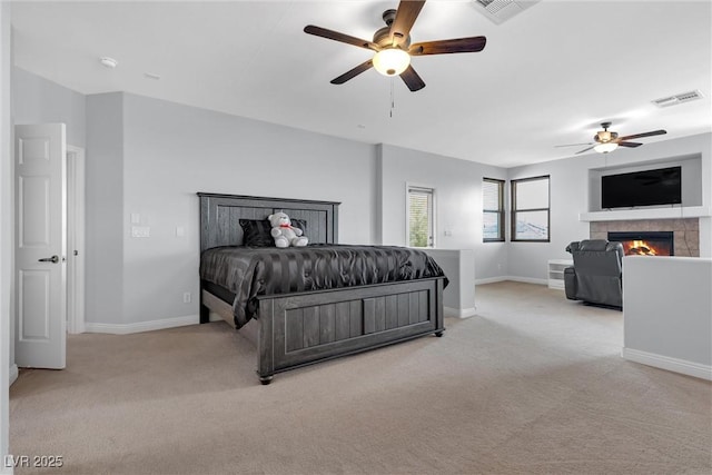 bedroom featuring light carpet, a tiled fireplace, and ceiling fan