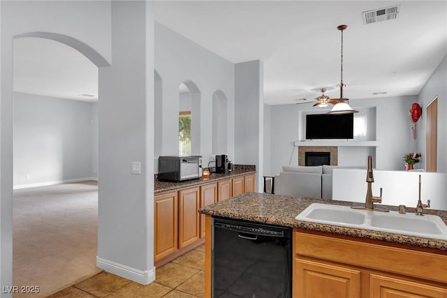 kitchen featuring black dishwasher, dark stone countertops, sink, a tiled fireplace, and light tile patterned floors