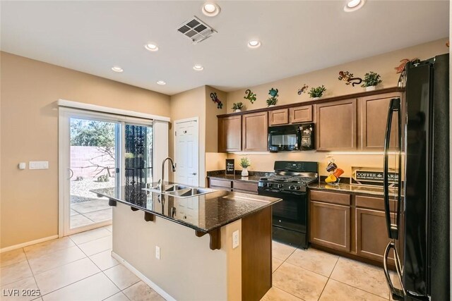 kitchen featuring sink, a breakfast bar area, a center island with sink, dark stone countertops, and black appliances