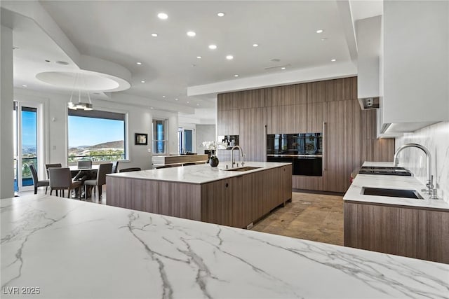 kitchen featuring sink, backsplash, decorative light fixtures, and a center island with sink