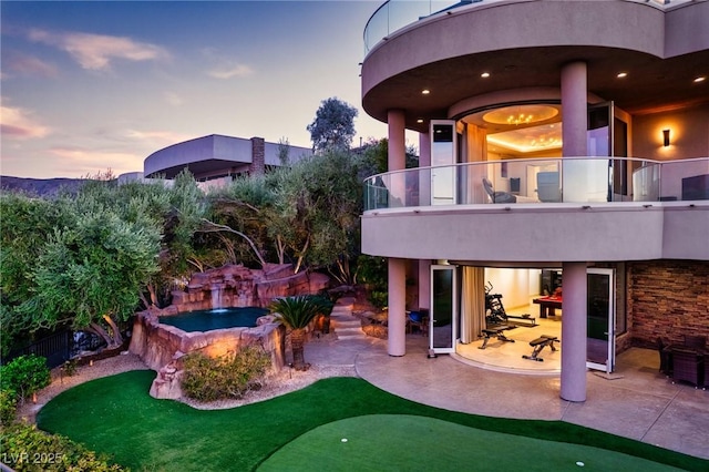 back house at dusk featuring a patio and a balcony