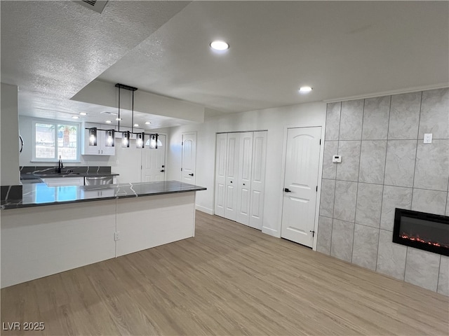 kitchen featuring light hardwood / wood-style flooring, white cabinets, a tiled fireplace, decorative light fixtures, and kitchen peninsula