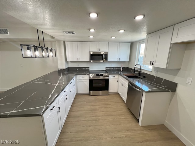 kitchen featuring sink, appliances with stainless steel finishes, white cabinetry, hanging light fixtures, and light hardwood / wood-style floors