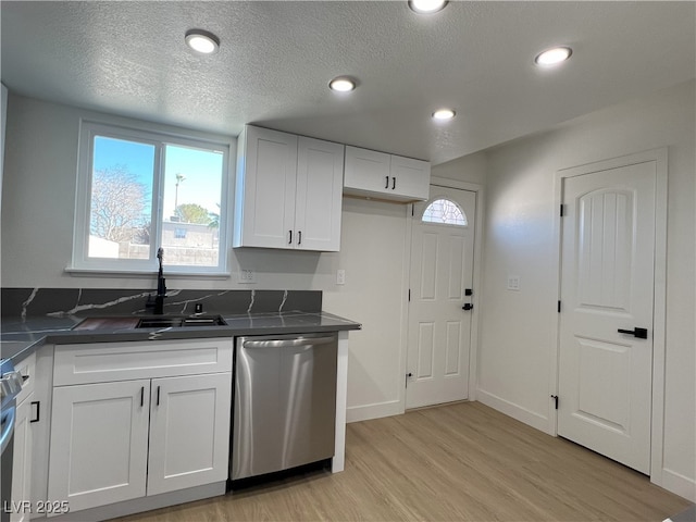 kitchen with sink, light wood-type flooring, white cabinets, stainless steel dishwasher, and a textured ceiling